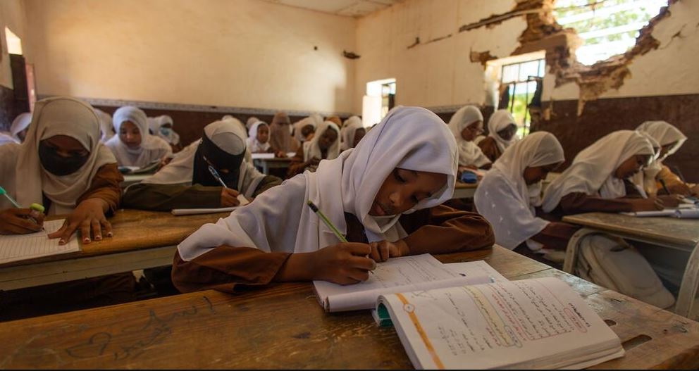 Students attend class in a damaged school building with cracked walls, illustrating climate-related disruptions to education.
