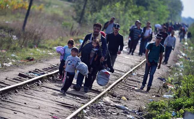 Migrants, including families with children, walking along railway tracks carrying belongings during a journey toward Europe