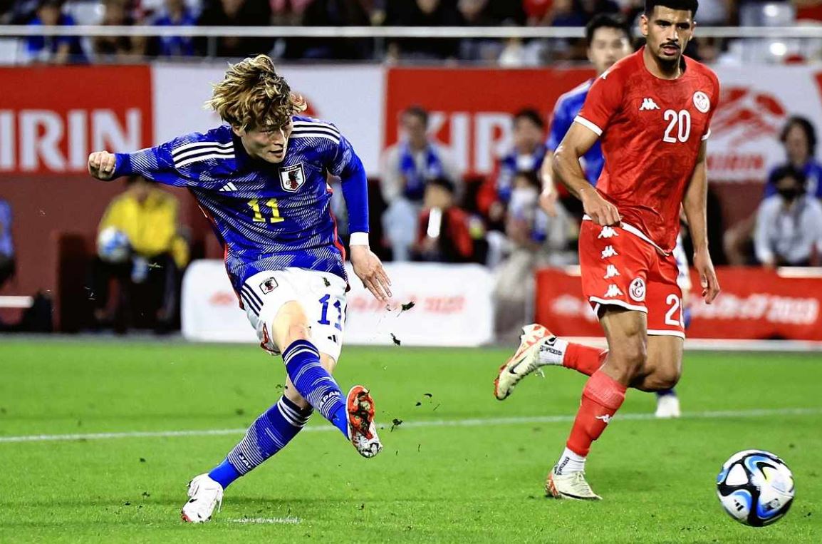 A Japan player takes a shot while a Tunisia defender closes in during an international football match before the FIFA World Cup 2026 clash.