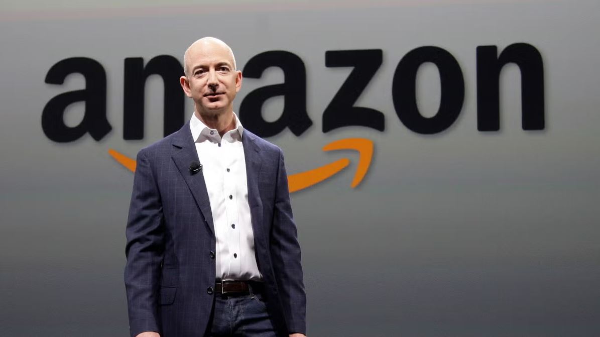 Jeff Bezos speaking in front of the Amazon logo during a company presentation on technology, AI innovation, and global business expansion.