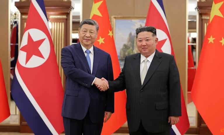 Xi Jinping of China and Kim Jong Un of North Korea shaking hands during a formal diplomatic meeting with national flags in the background.