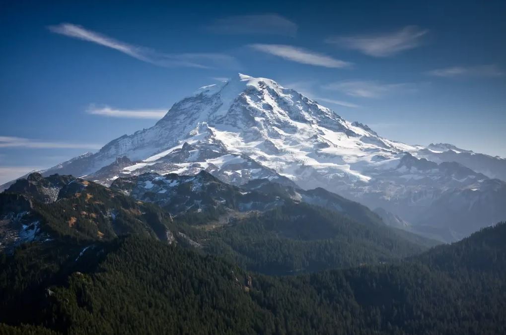 Mount Rainier, an active volcano in Washington State, towering above forested valleys that face potential lahar (volcanic mudflow) risk zones.