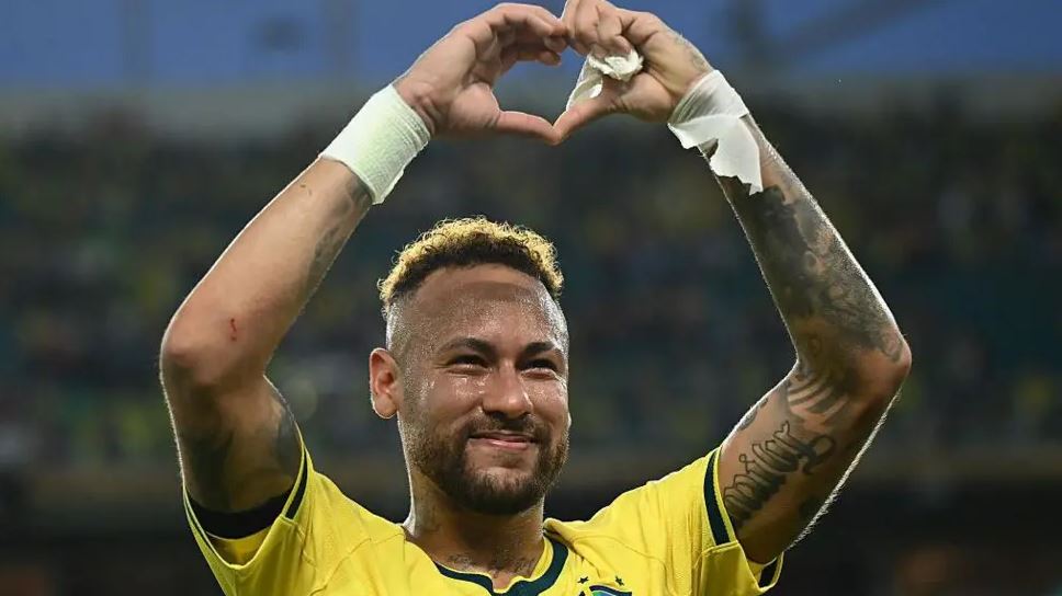 Brazilian football player Neymar celebrates during a 2026 FIFA World Cup match, forming a heart shape with his hands while wearing Brazil's yellow jersey.