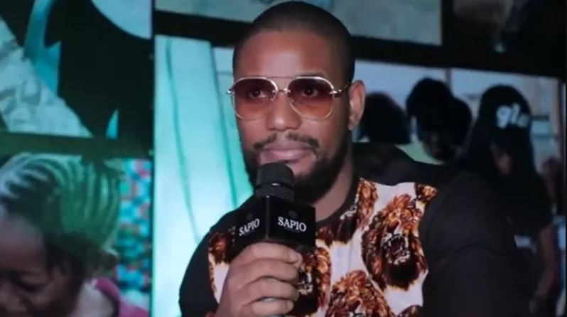 Nollywood actor Alexx Ekubo speaking into a microphone during a public event before his death at age 40.