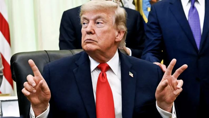 Donald Trump seated at a White House meeting wearing a suit and red tie.