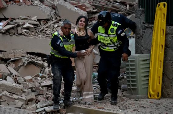 Police officers help a woman walk through debris and collapsed buildings following the deadly Venezuela earthquake in Caracas.